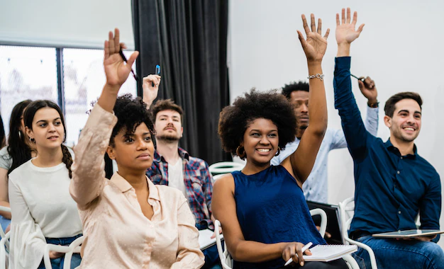 A group of people sitting in chairs raising their hands.