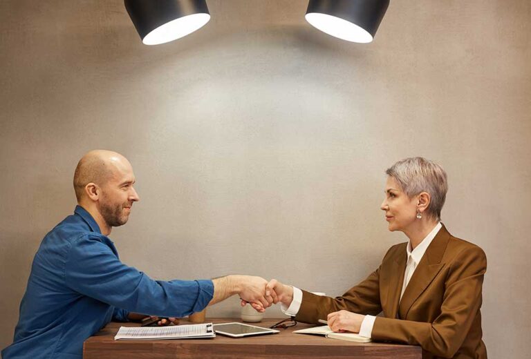 Two people shaking hands over a table.