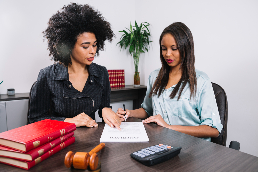 Two women sitting at a table with papers and a judge 's gavel.